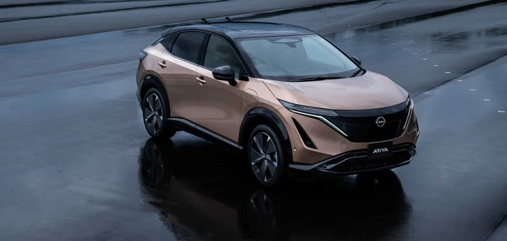 Nissan Ariya cuivrée à toit noir en trois quarts avant, vue en hauteur sur une piste mouillée