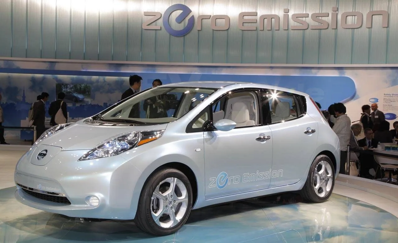 Nissan LEAF argent bleuté exposée sur un stand portant l'inscription « Zero Emission », avec des visiteurs derrière