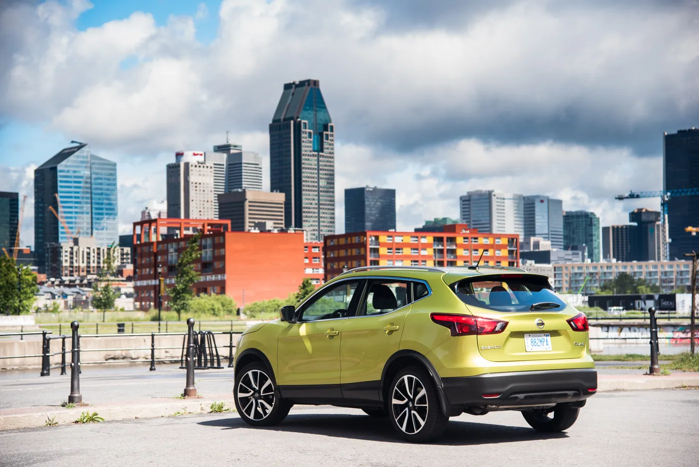 Nissan Qashqai vert lime en trois quarts arrière, devant les gratte-ciel du centre-ville de Montréal