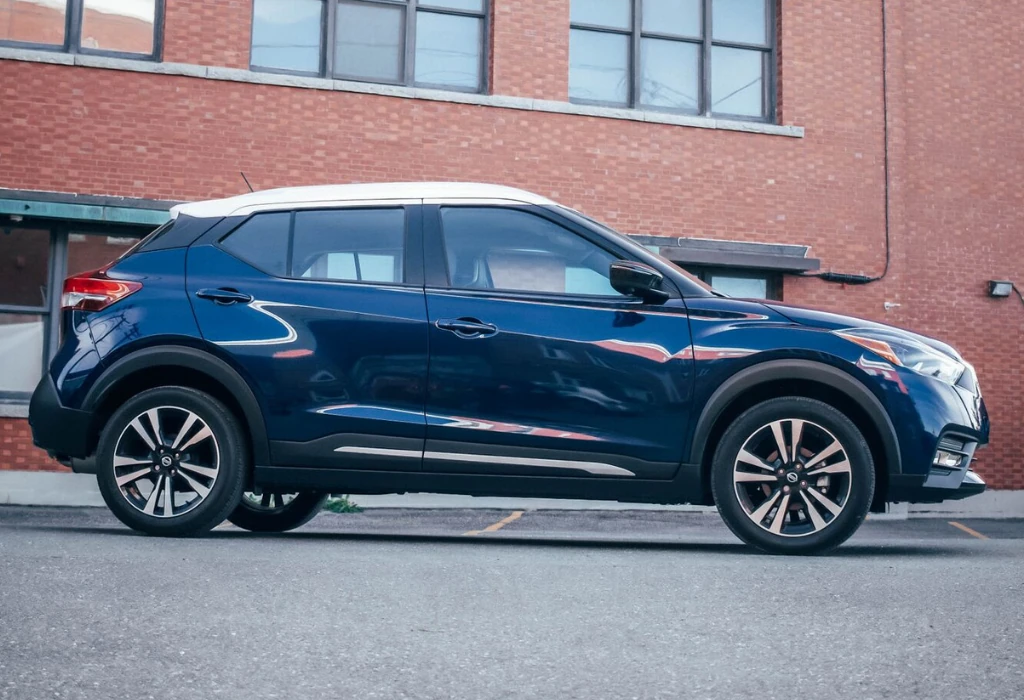 Nissan Kicks bleu foncé à toit blanc, vue de profil devant un bâtiment en brique