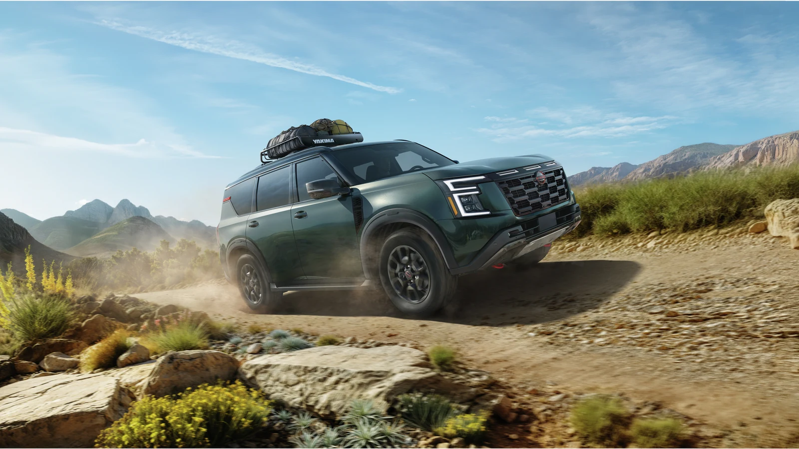 Nissan Armada vert foncé roulant sur un sentier de terre et de roches, montagnes en arrière-plan