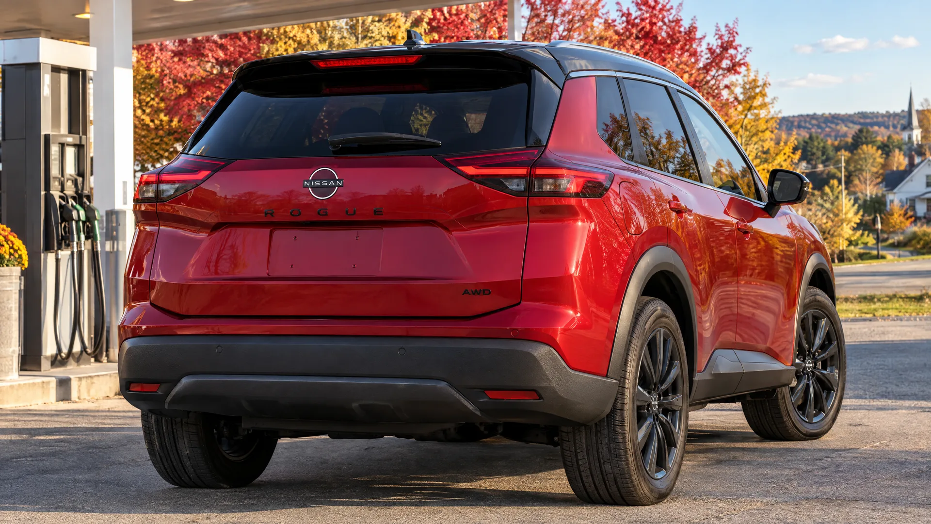 Nissan Rogue 2026 rouge vu de trois quarts arrière près d'une station-service de village des Cantons-de-l'Est, soleil bas de fin d'après-midi