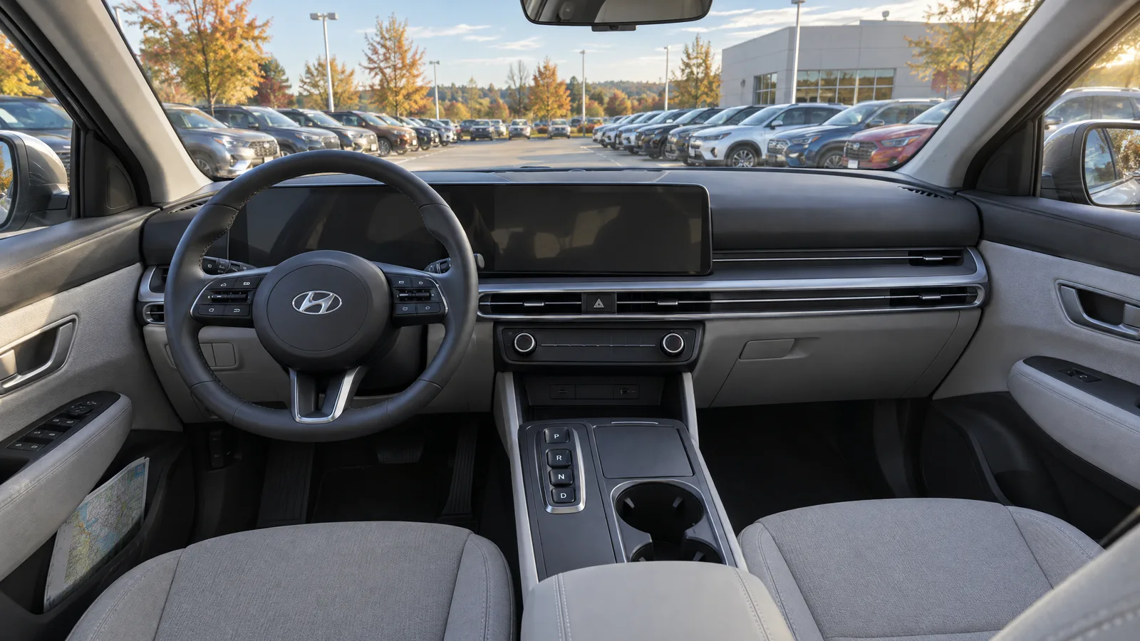 Habitacle d'un Hyundai Tucson 2026 vu depuis le siège passager, écran central en veille, sellerie grise et coutures apparentes, stationnement de concession par le pare-brise