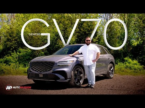 Voir l'essai vidéo du Genesis GV70 2026 gris, vu de trois quarts avant devant un boisé, un essayeur appuyé sur le capot