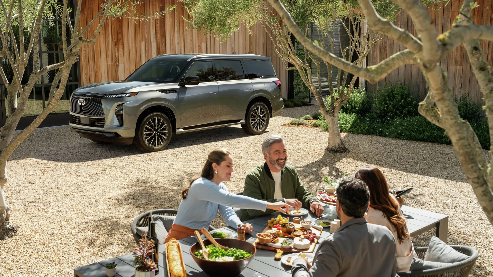 Famille attablée pour un repas en plein air devant un INFINITI QX80 gris