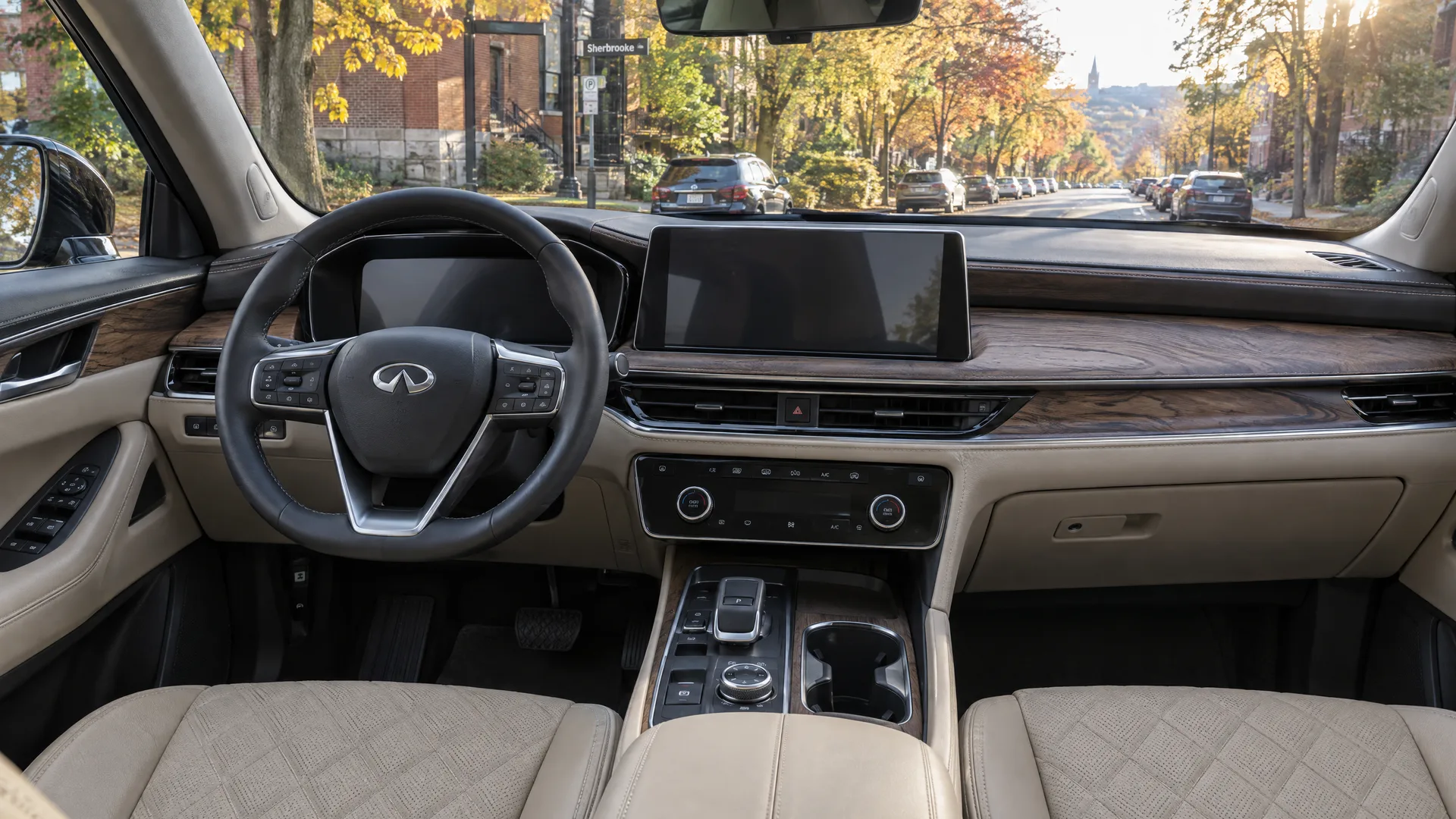 Habitacle d'un INFINITI QX60 2026 vu depuis le siège passager avant, écrans éteints, sellerie de cuir pâle matelassée, boiseries à pores ouverts