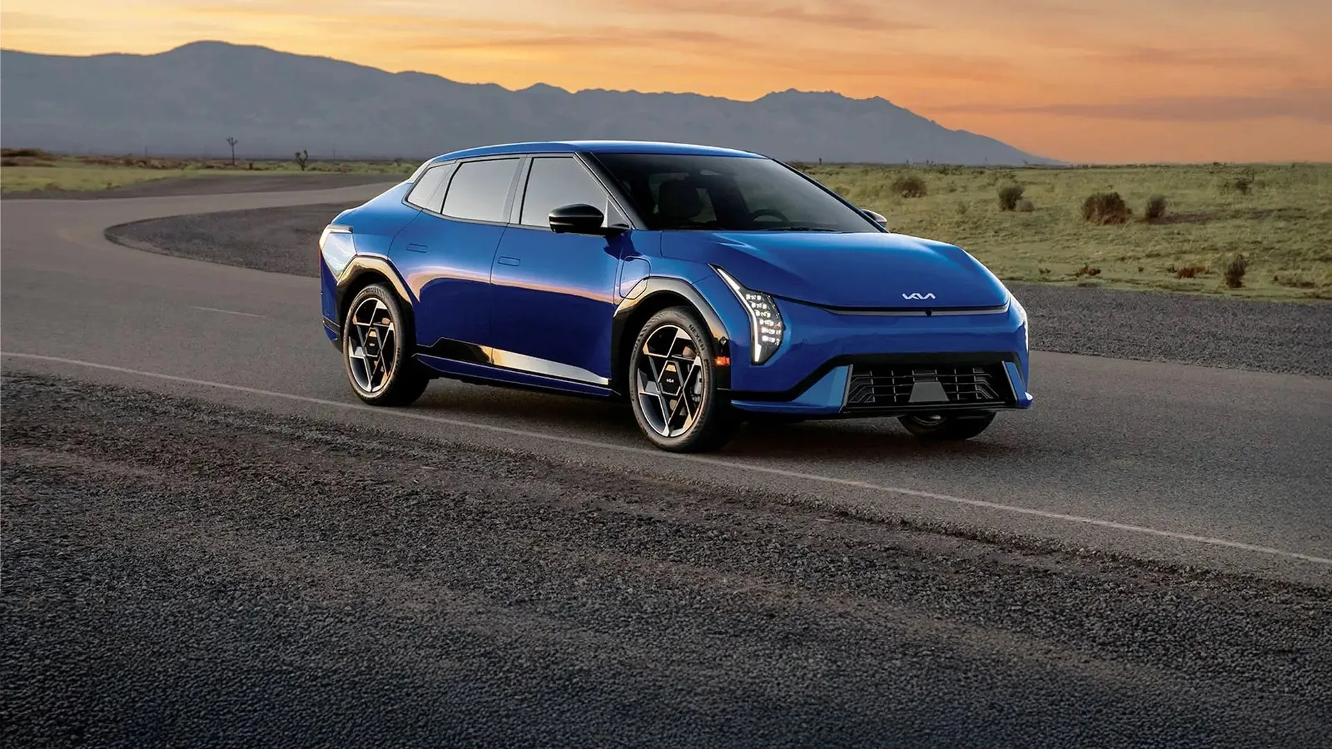 Kia EV4 bleu sur une route de campagne au crépuscule, montagnes à l'horizon