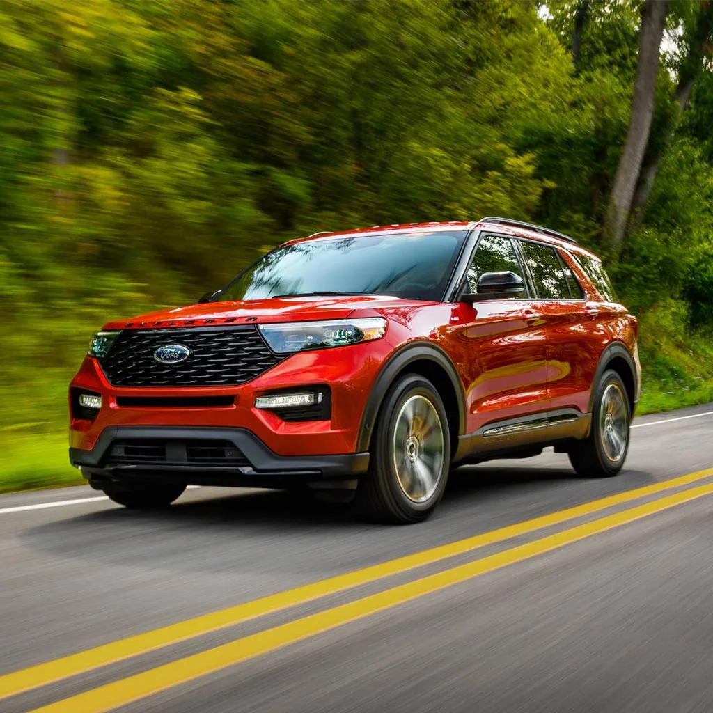 Ford Explorer 2023 rouge en mouvement sur une route bordée d'arbres, vue de trois quarts avant