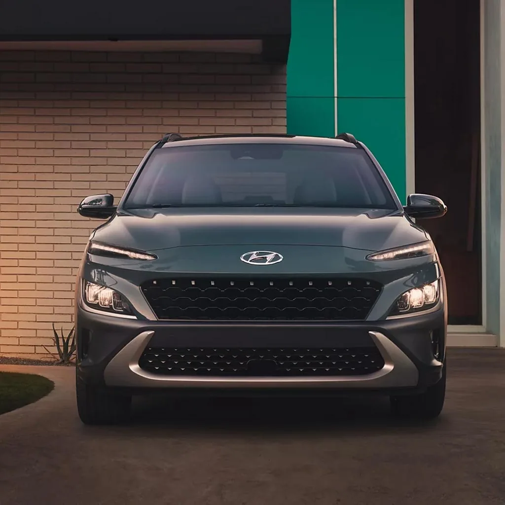 Hyundai Kona 2023 gris-vert vu de face devant un mur de briques