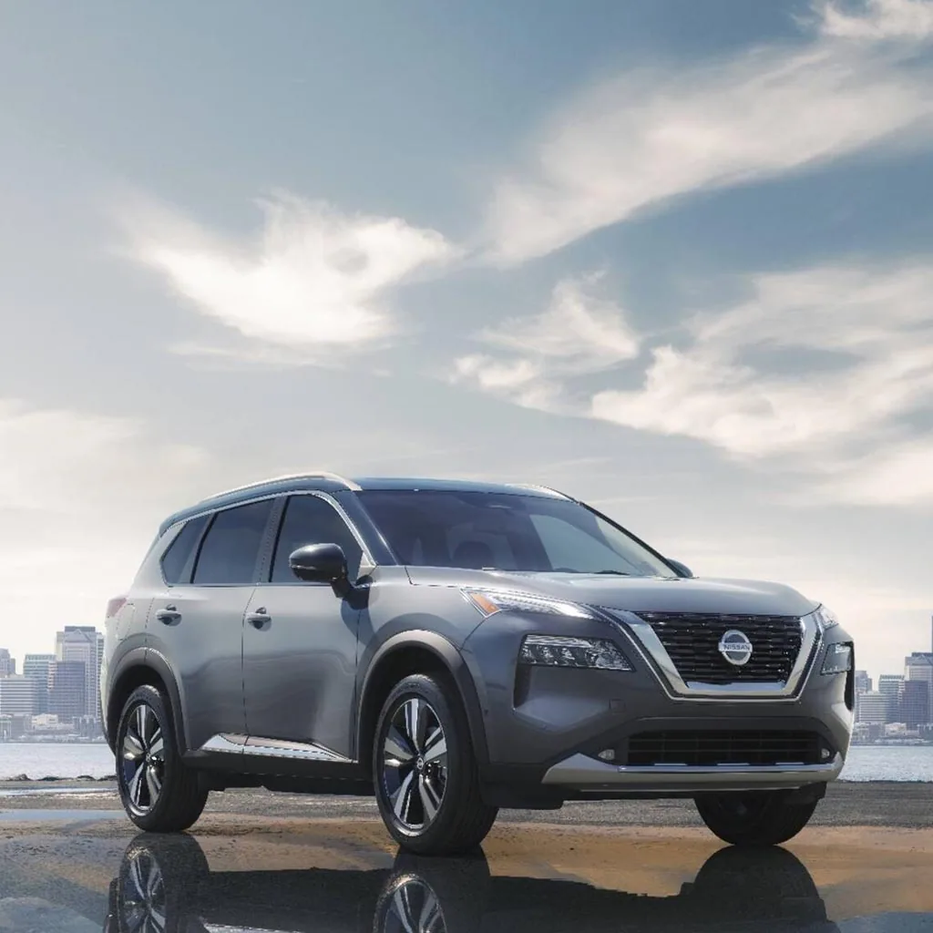Nissan Rogue 2023 gris vu de trois quarts avant au bord de l'eau, ville en arrière-plan