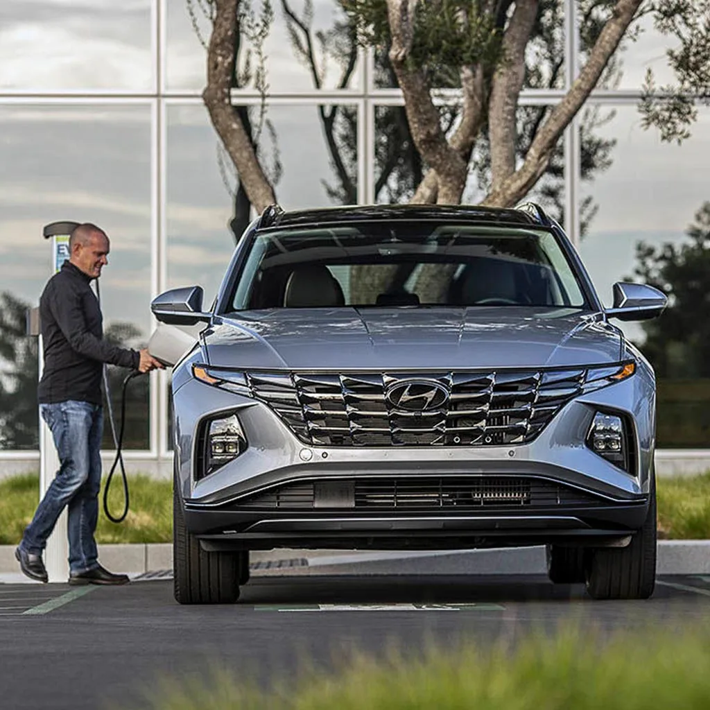 Hyundai Tucson PHEV 2023 gris vu de face pendant qu'un homme branche le câble de recharge