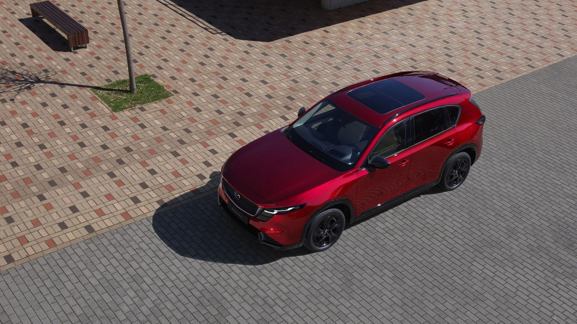 Mazda CX-5 2026 rouge vu en plongée, stationné sur une place pavée, toit ouvrant et emblème Mazda visibles