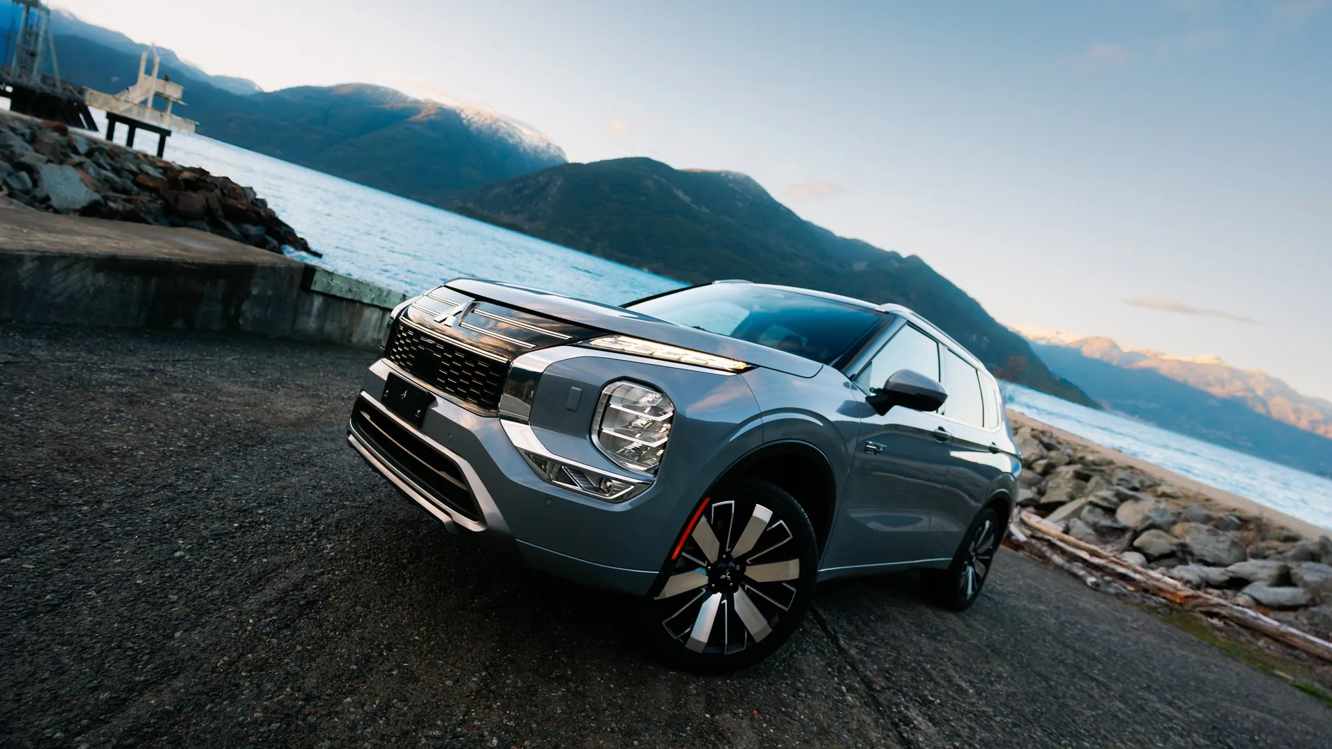 Mitsubishi Outlander PHEV 2026 gris stationné au bord d'un fjord entouré de montagnes enneigées