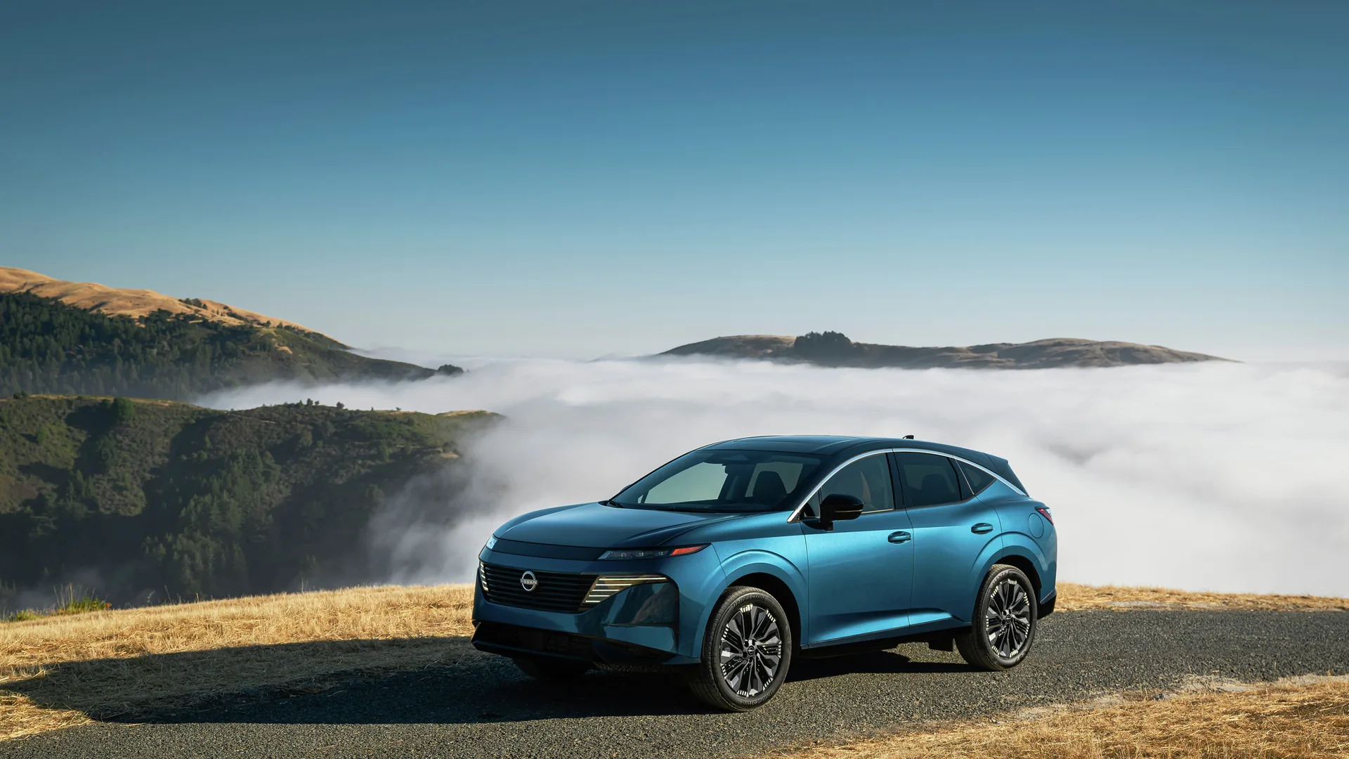 Nissan Murano bleu stationné sur une crête de montagne au-dessus d'une mer de nuages, sous un ciel dégagé
