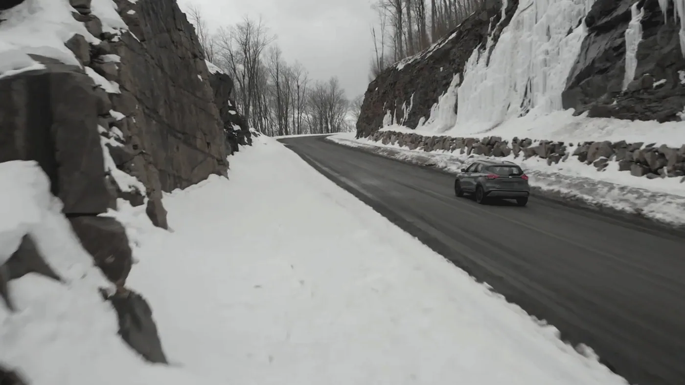 Nissan Kicks 2021 gris vu de l'arrière sur une route de montagne enneigée entre un mur de roche et de la glace