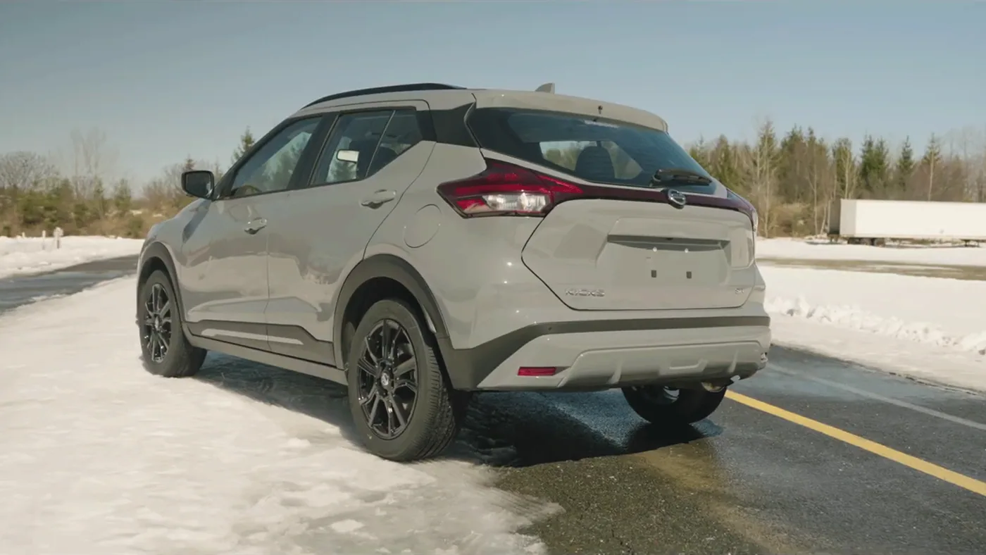 Nissan Kicks 2021 gris pâle vu de trois quarts arrière avec jantes noires, sur une route bordée de neige