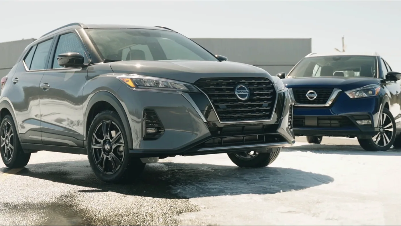 Nissan Kicks 2021 gris vu de l'avant, avec l'ancien Kicks bleu en arrière-plan, sur sol enneigé
