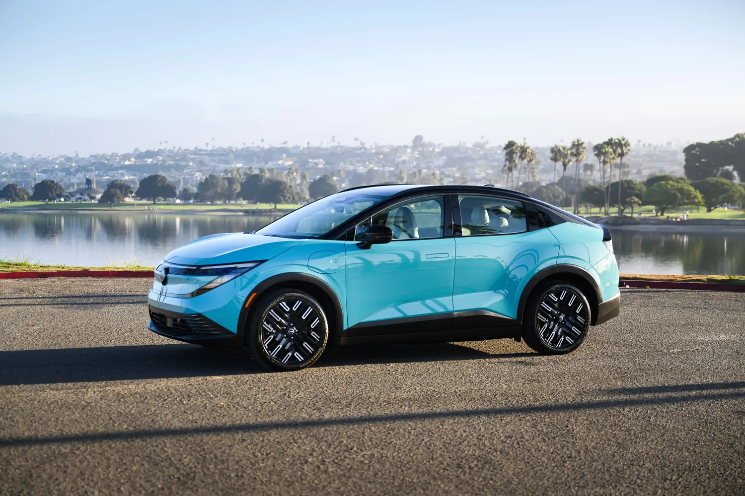 Nissan LEAF bleu clair de profil devant un plan d'eau et des palmiers