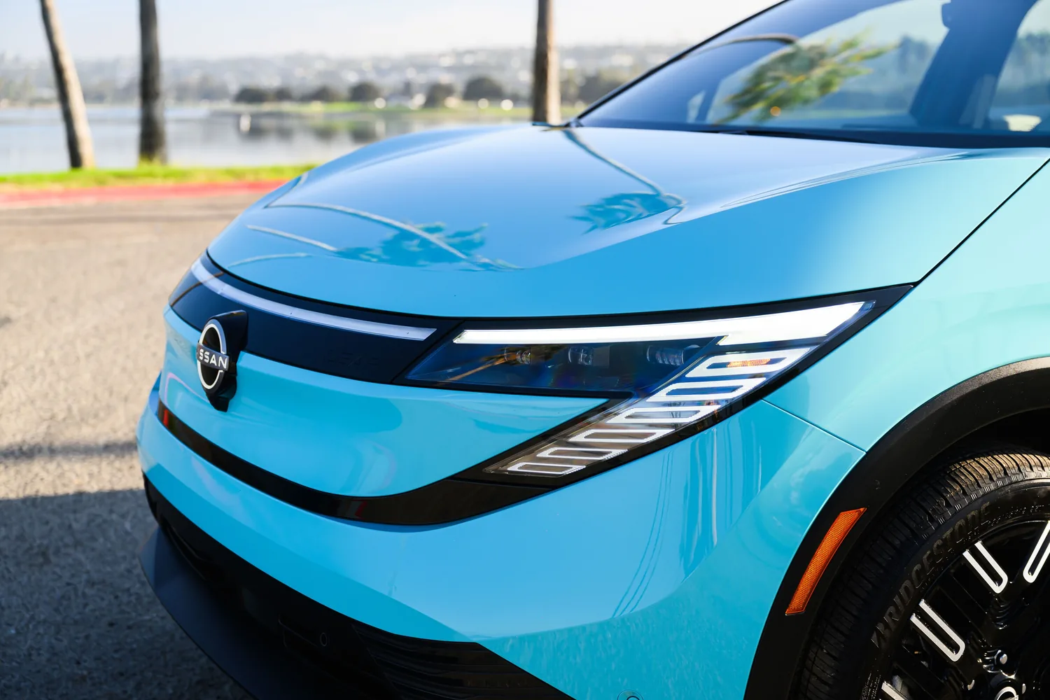 Gros plan sur la face avant d'une Nissan LEAF bleu clair : emblème Nissan éclairé et bandeau lumineux