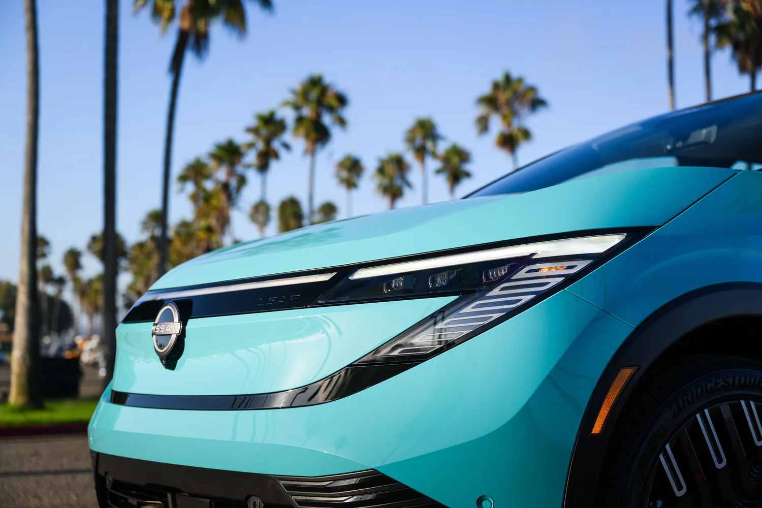 Nissan LEAF bleu clair de trois quarts avant, stationnée sous des palmiers