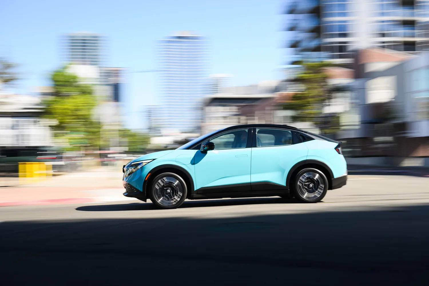 Nissan LEAF bleu clair en mouvement dans une rue de centre-ville, immeubles flous en arrière-plan