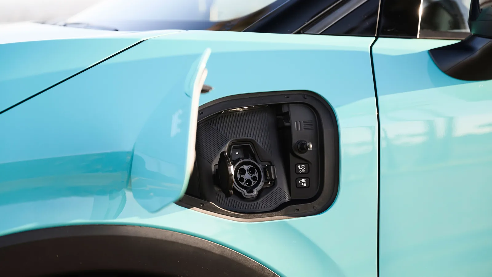 Gros plan sur le port de recharge ouvert d'une Nissan LEAF bleu clair, avec sa prise de recharge et sa trappe