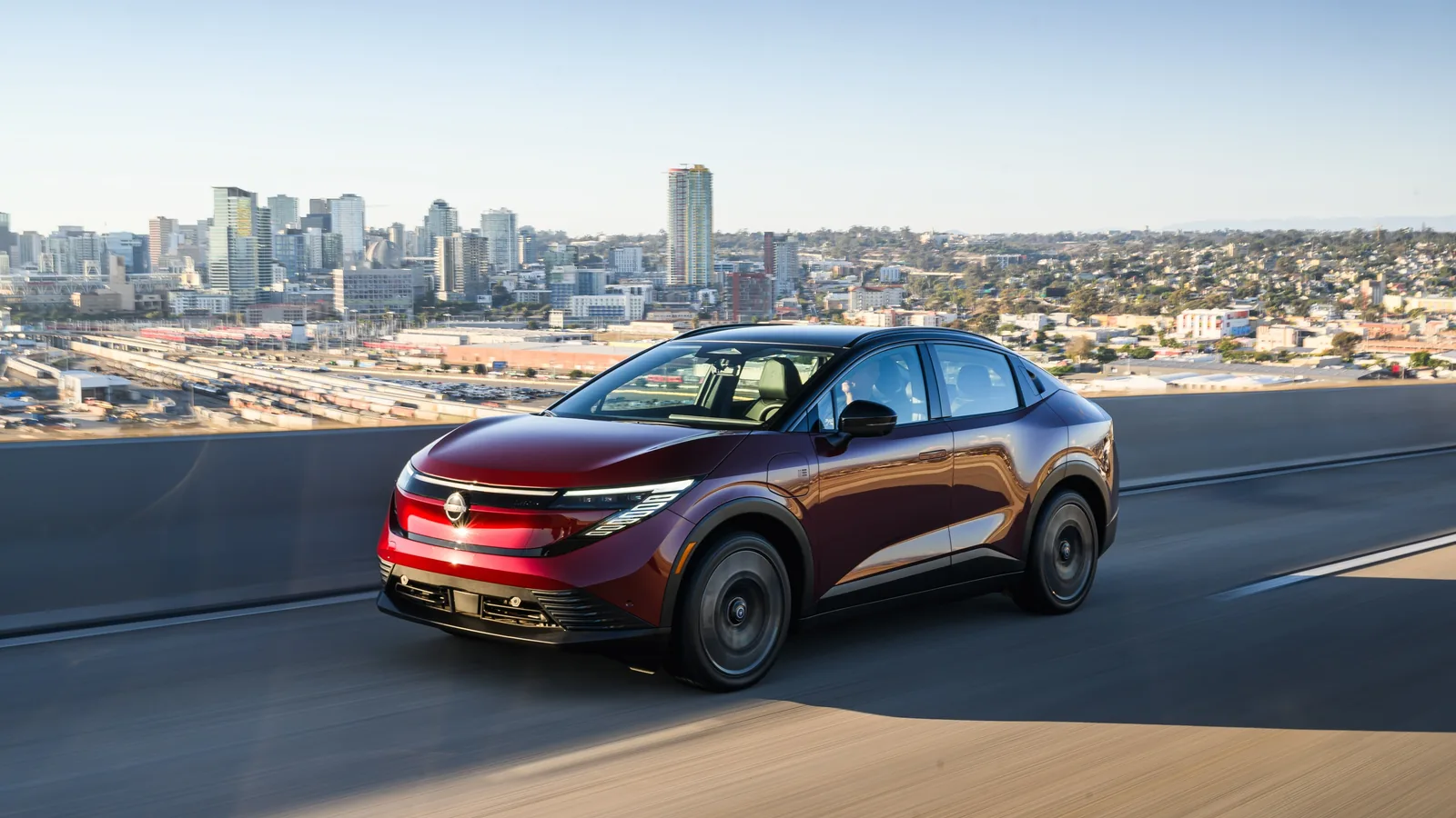 Nissan LEAF rouge vue de trois quarts arrière sur une route côtière avec une ville en arrière-plan