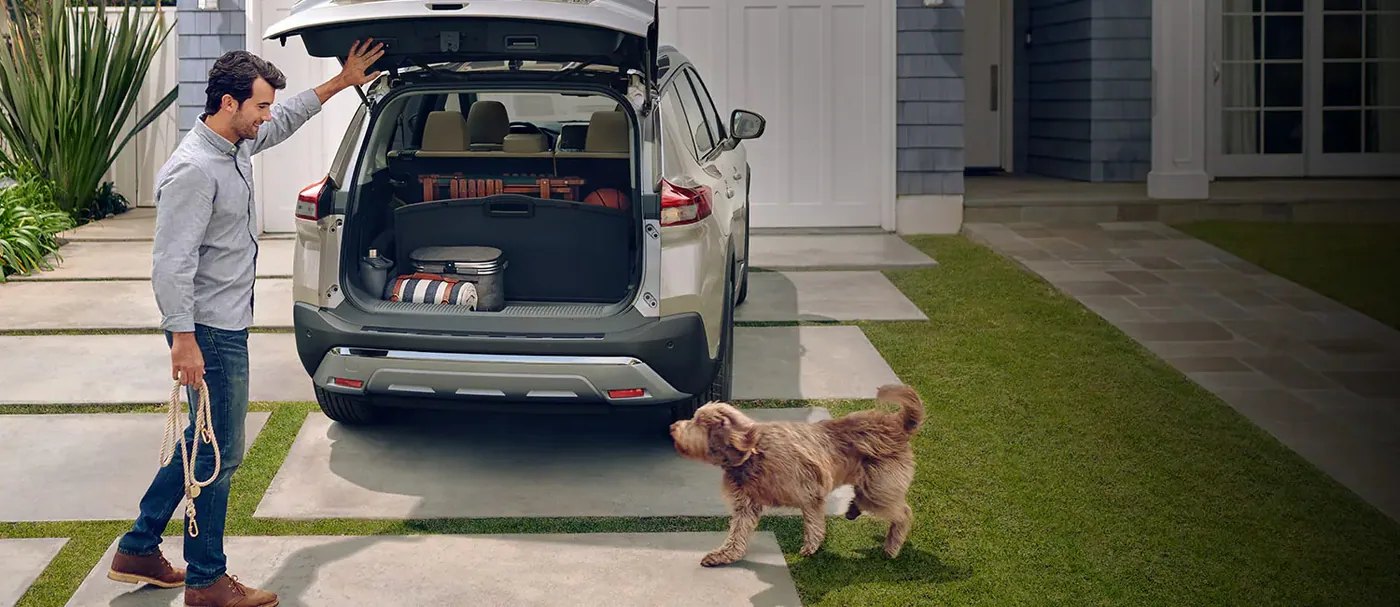 Coffre ouvert et chargé d'un Nissan Rogue 2023, avec un homme tenant une laisse et un chien dans l'entrée