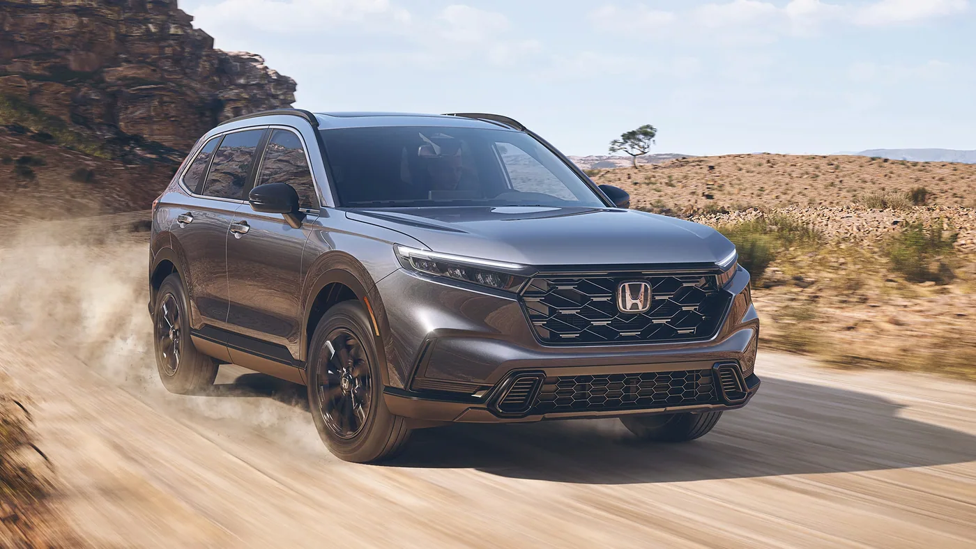 Honda CR-V 2023 gris métallisé roulant sur un chemin de terre en soulevant de la poussière, trois quarts avant