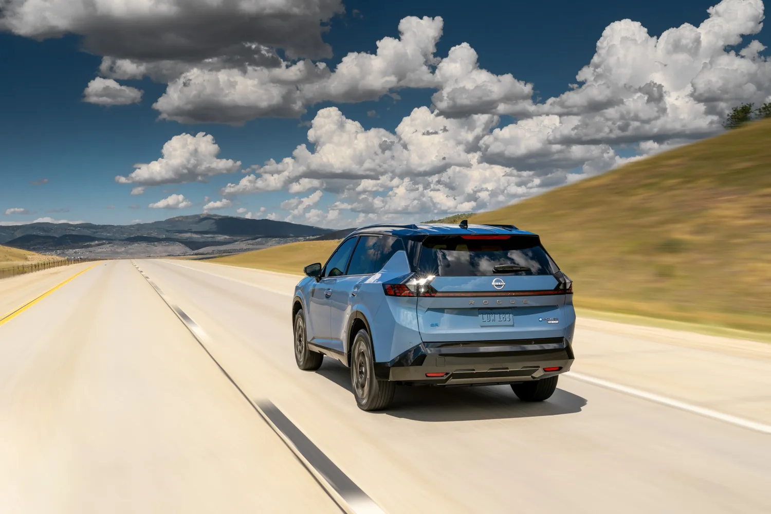 Nissan Rogue hybride 2027 bleu roulant sur une autoroute déserte sous un ciel de cumulus