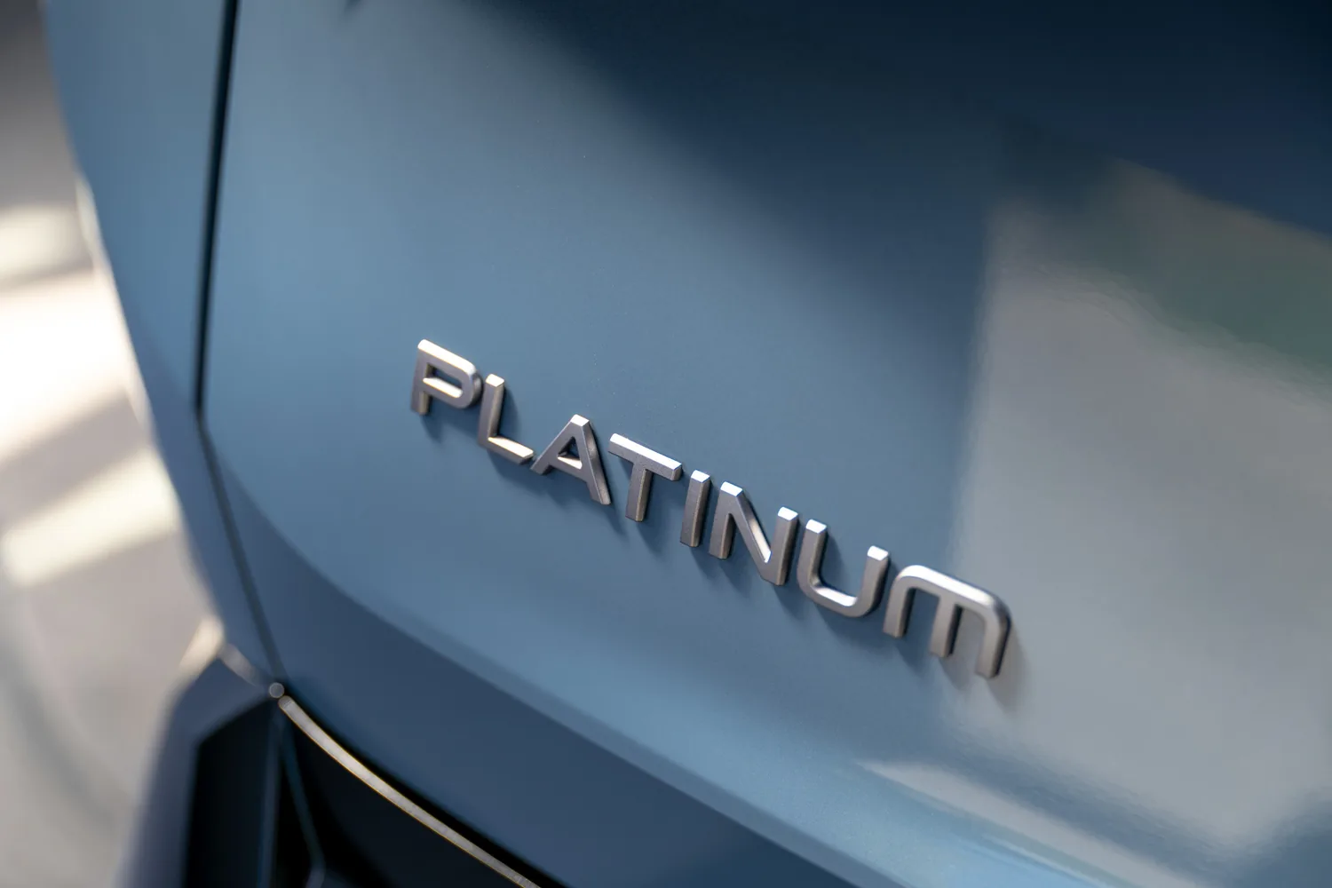 Écusson Platinum en lettres chromées sur la carrosserie bleue d'un Nissan Rogue hybride 2027
