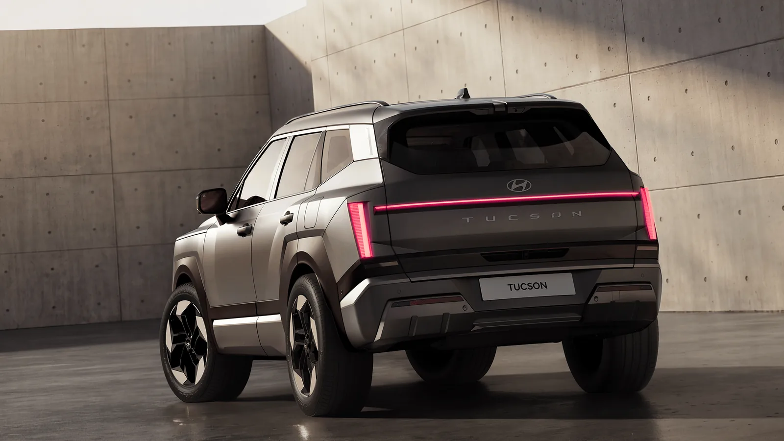 Nouveau Hyundai Tucson gris taupe vu de trois quarts arrière dans un studio de béton