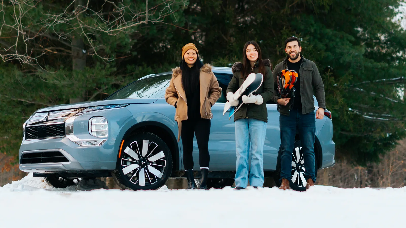 Trois amis avec planche à neige et casque devant un Mitsubishi Outlander bleu pâle stationné dans la neige