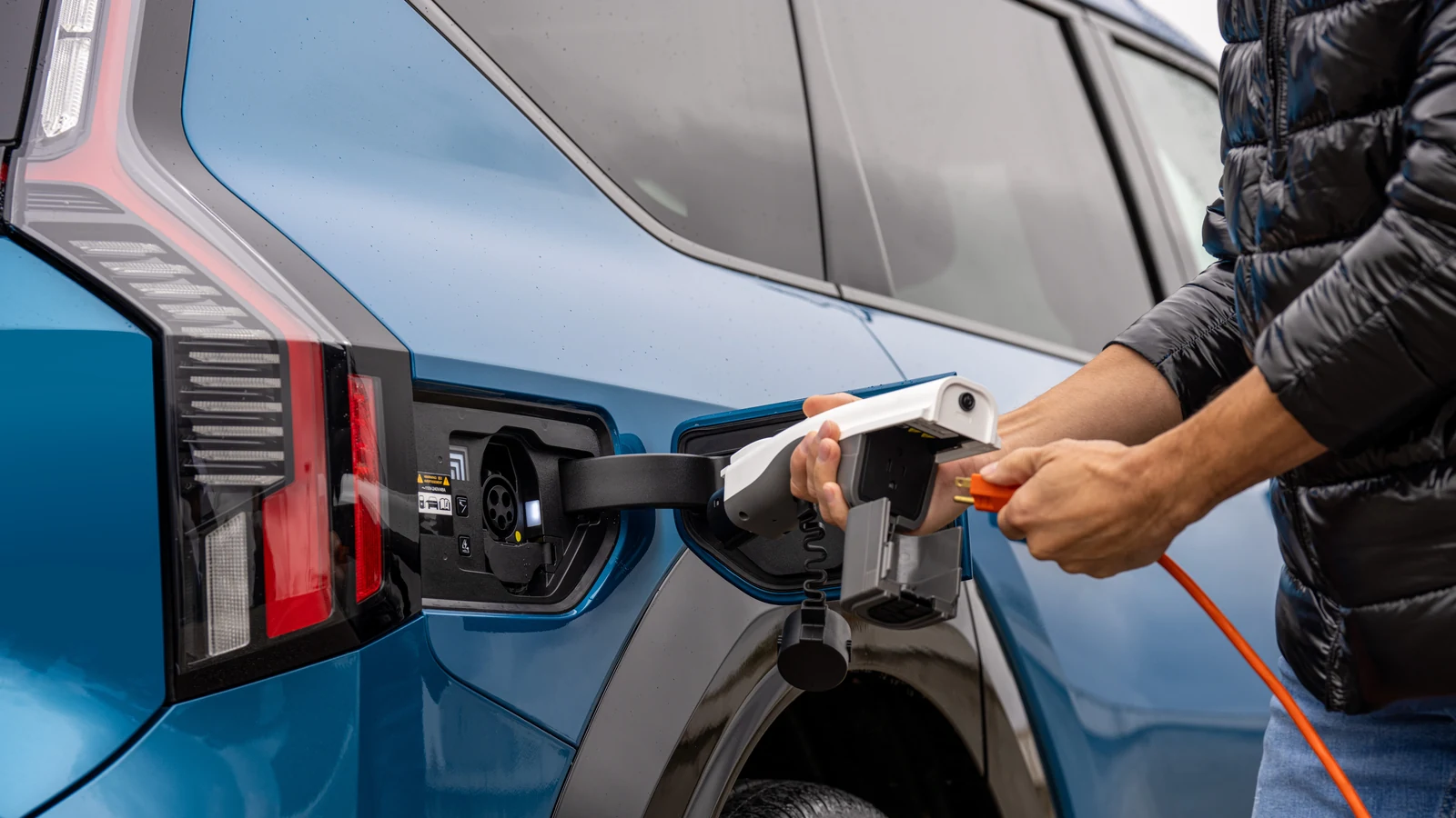 Main qui insère le connecteur de recharge dans le port d'un Kia EV9 bleu