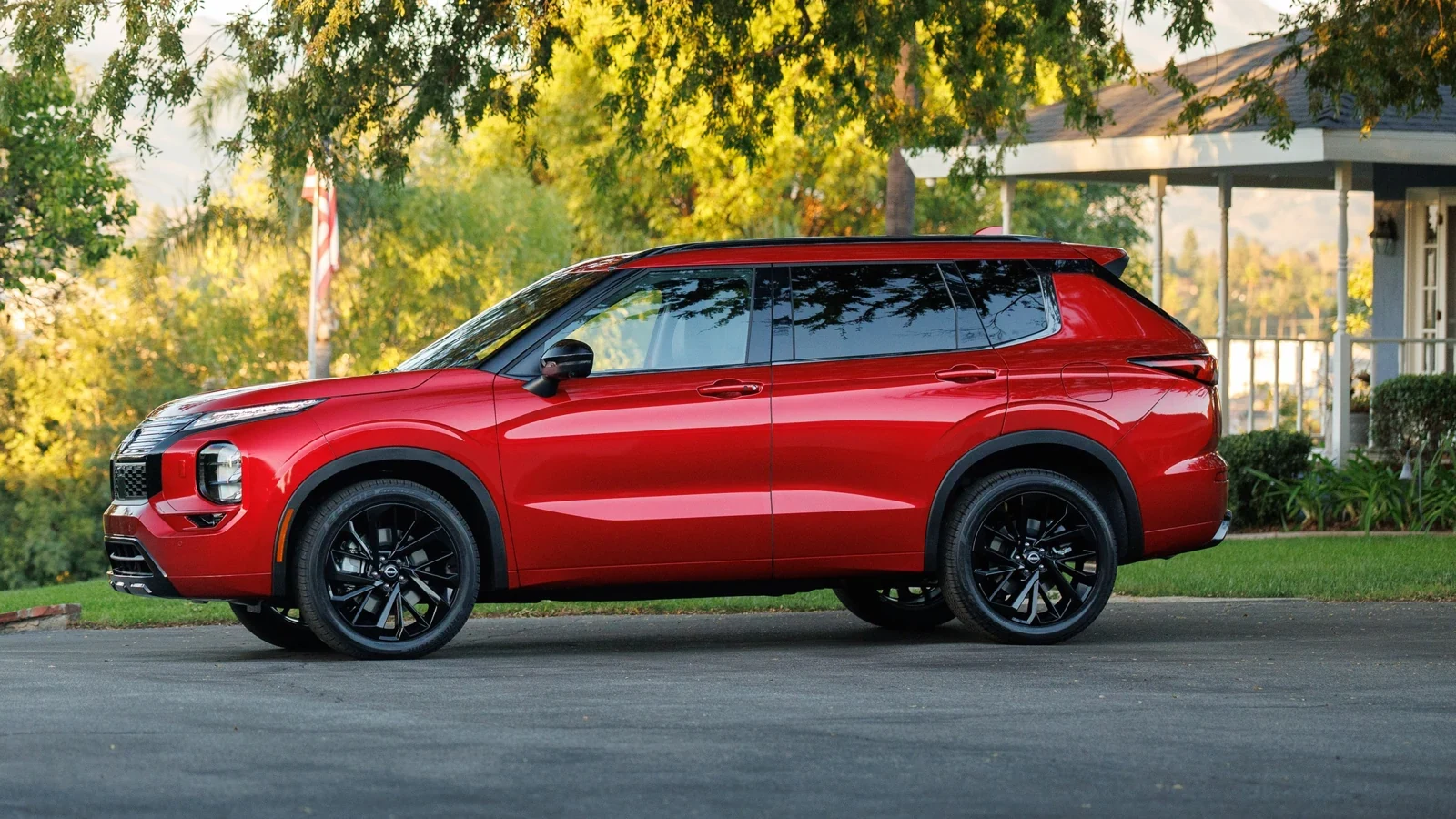 Nissan Rogue hybride rechargeable rouge vu de profil, stationné dans une entrée sous les arbres