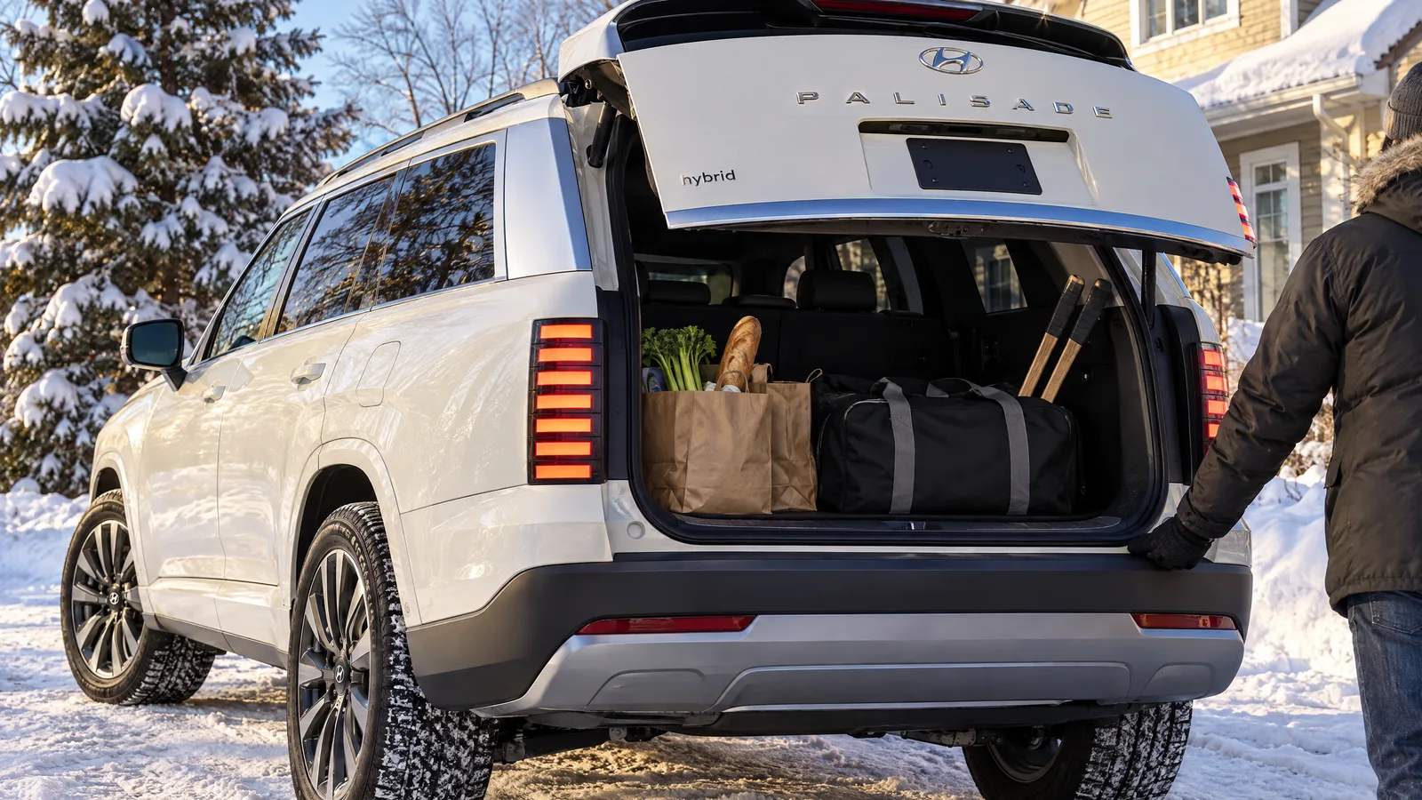 Hyundai Palisade hybride 2026 blanc, hayon ouvert, sacs d'épicerie et équipement de hockey dans le coffre, entrée résidentielle québécoise ensoleillée en hiver