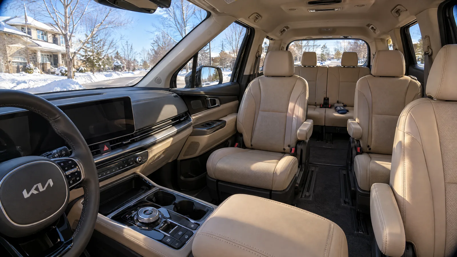 Habitacle d'un Kia Carnival HEV 2026 vu depuis le siège passager, écran central en veille, sellerie beige, troisième rangée visible à l'arrière