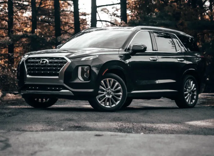 Hyundai Palisade noir, vue de trois quarts avant, sur un chemin bordé d'arbres aux couleurs d'automne