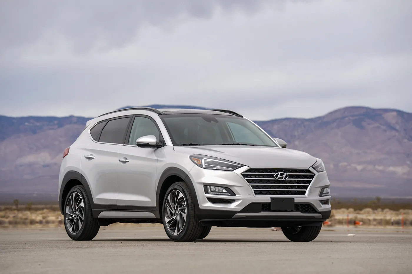 Hyundai Tucson gris argent, vue de trois quarts avant, devant des montagnes sous un ciel nuageux