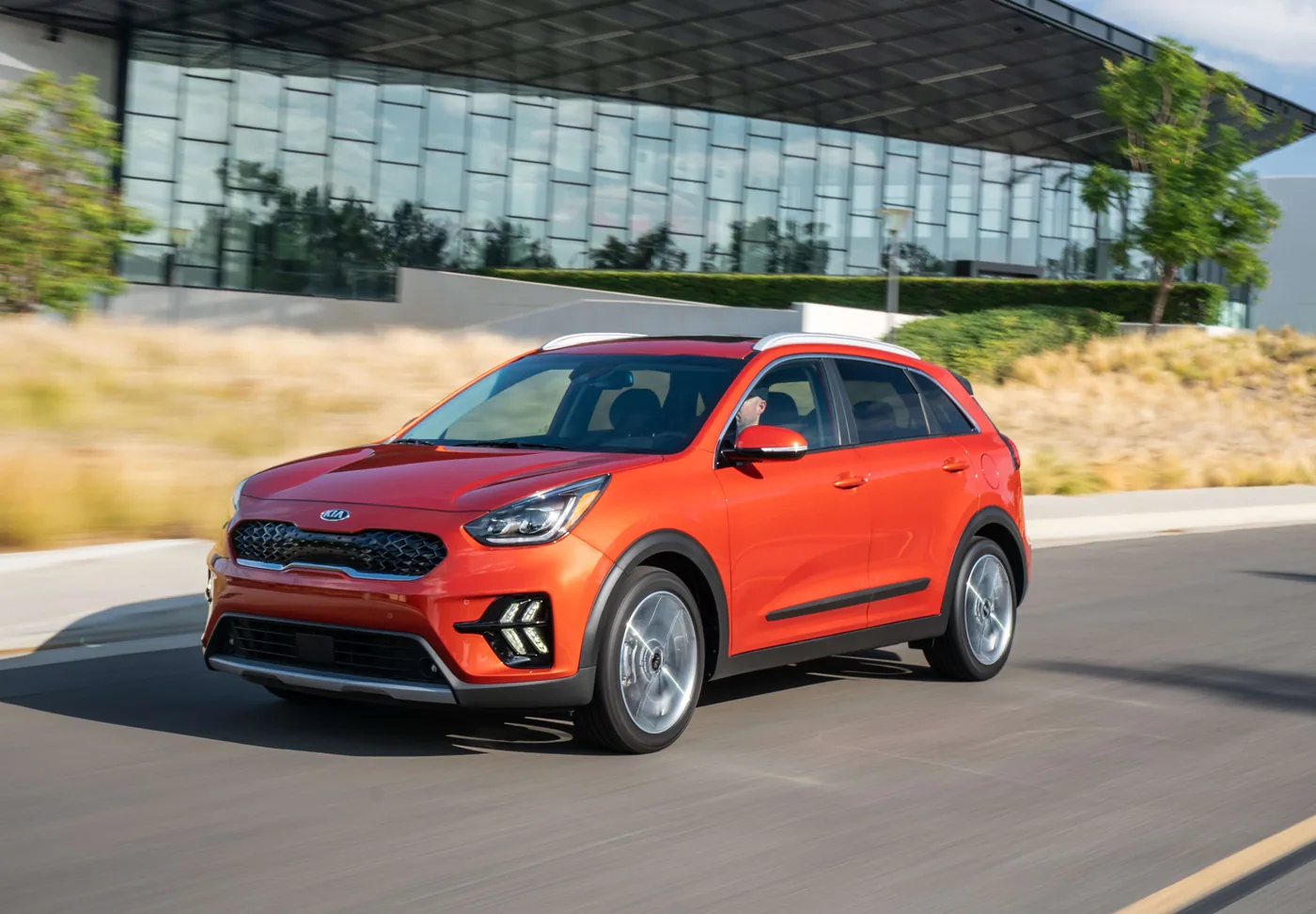 Kia Niro orange à toit blanc, en trois quarts avant, roulant devant un bâtiment vitré moderne