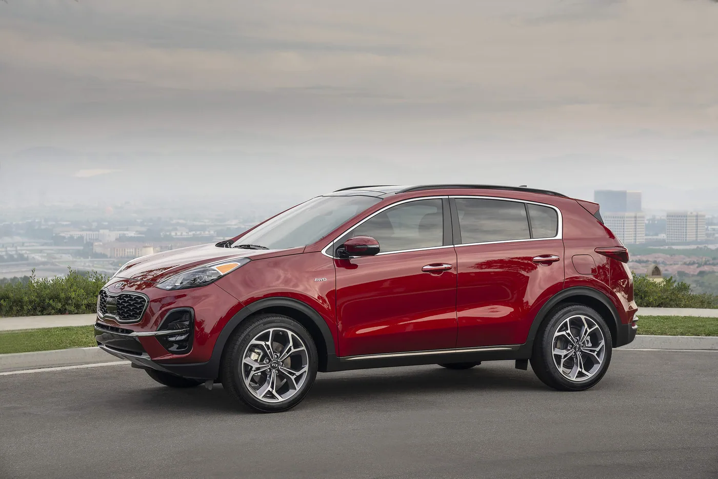 Kia Sportage rouge à traction intégrale, vu de profil, garé sur un belvédère avec la ville dans la brume
