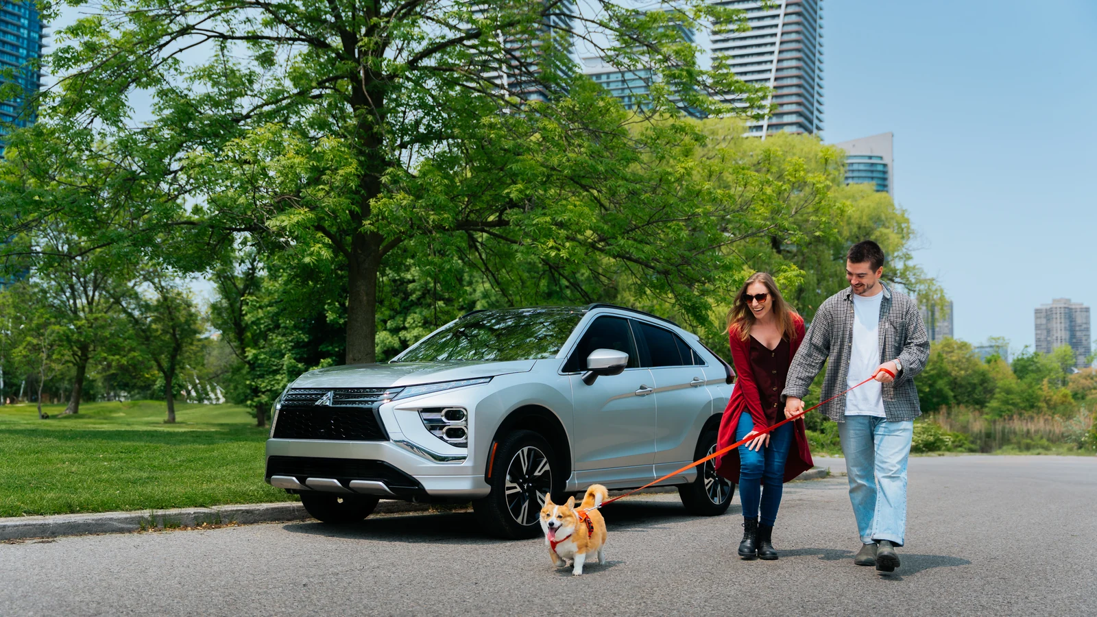 Couple promenant un petit chien près d'un Mitsubishi Eclipse Cross 2026 argent garé en bordure d'un parc