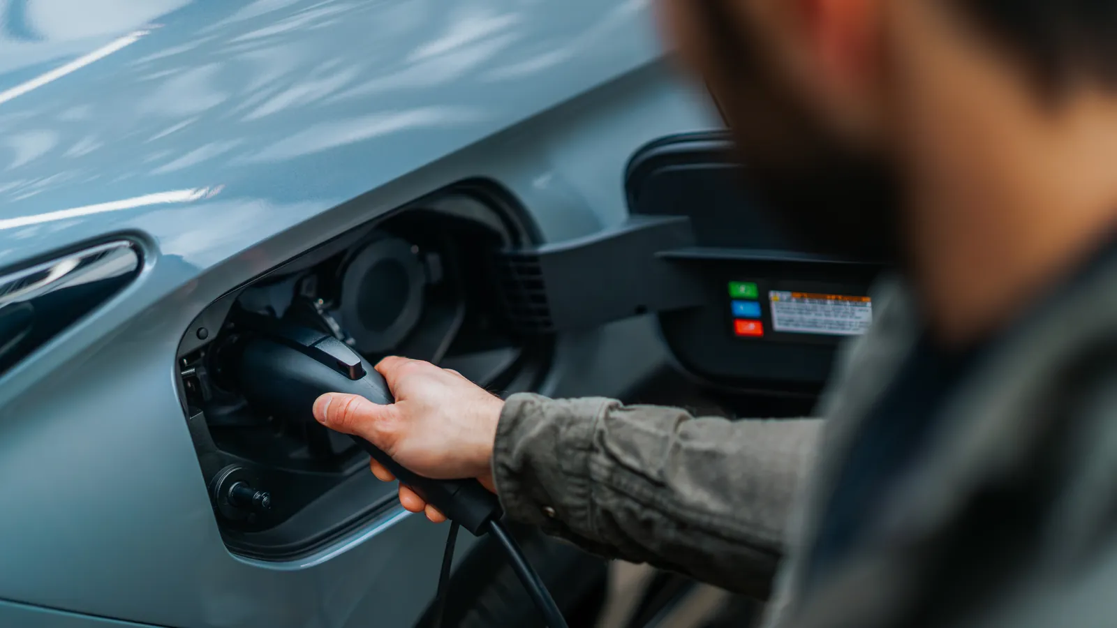 Un homme branche le câble de recharge dans la trappe d'un Mitsubishi Outlander PHEV 2026 gris