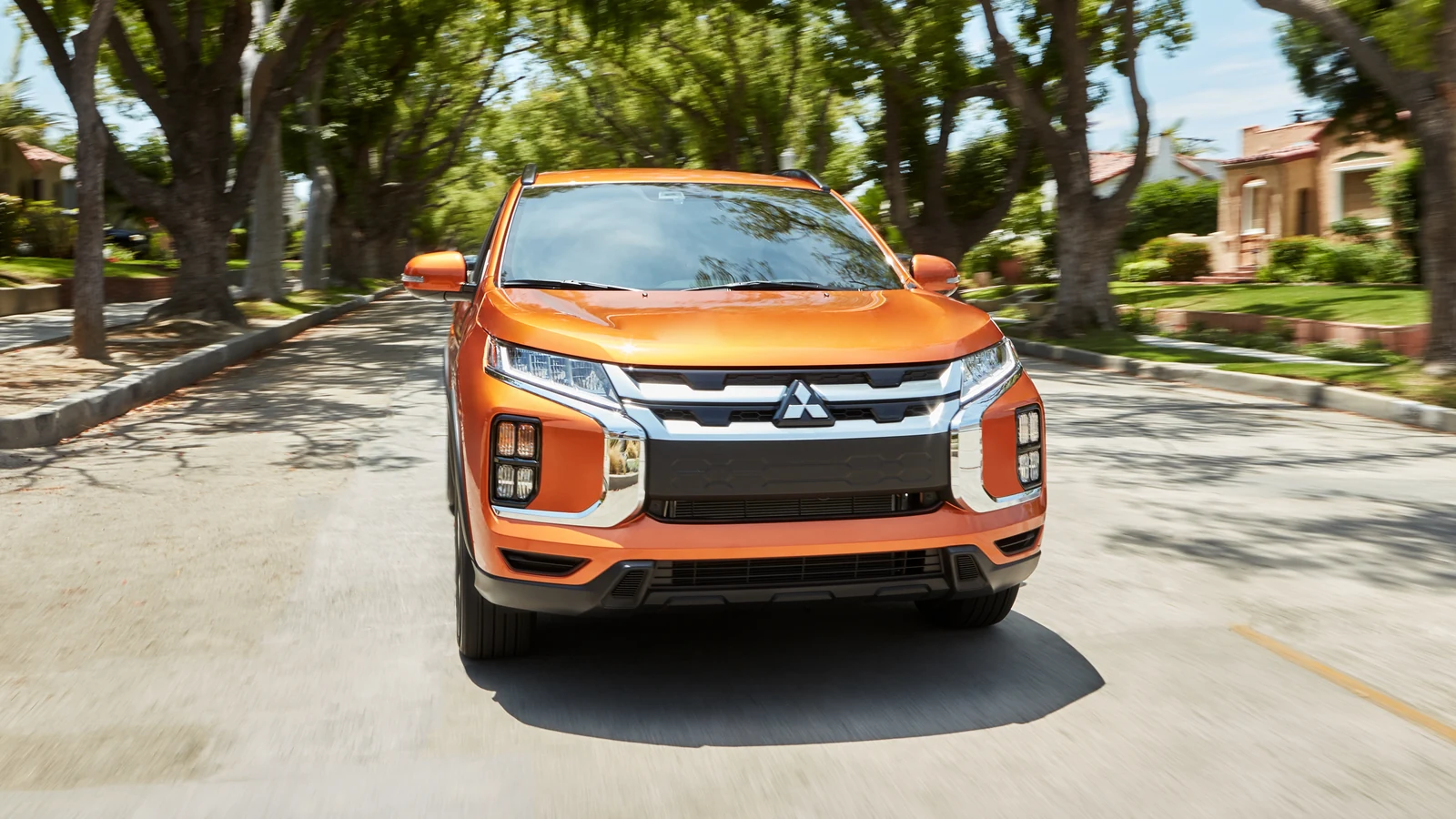 Mitsubishi RVR orange roulant de face dans une rue bordée d'arbres, emblème Mitsubishi au centre de la calandre