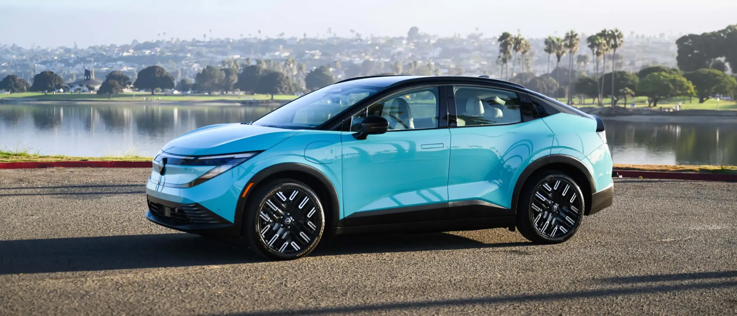 Nissan Leaf turquoise vue de trois quarts avant, stationnée au bord d’un lac par une journée ensoleillée.