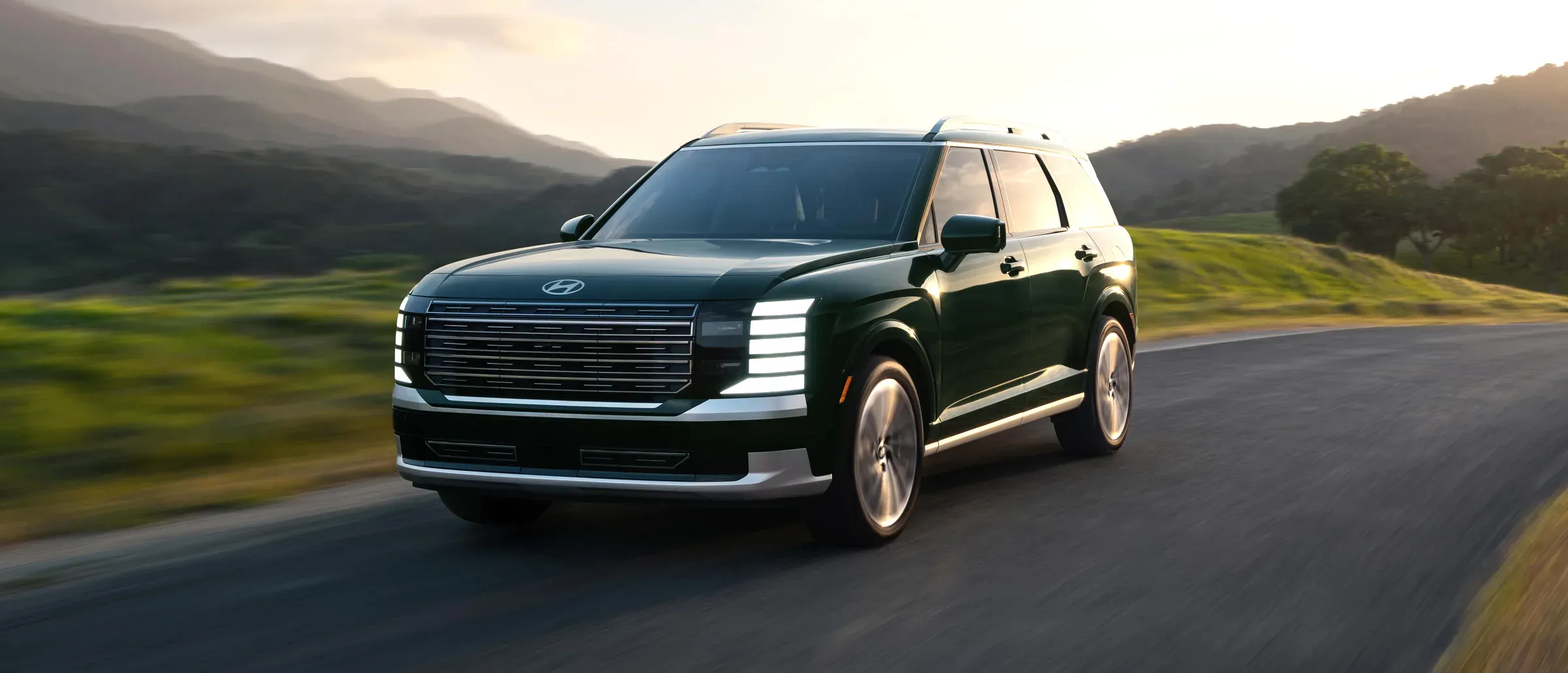 Hyundai Palisade vert foncé sur une route de campagne sinueuse, au soleil couchant.
