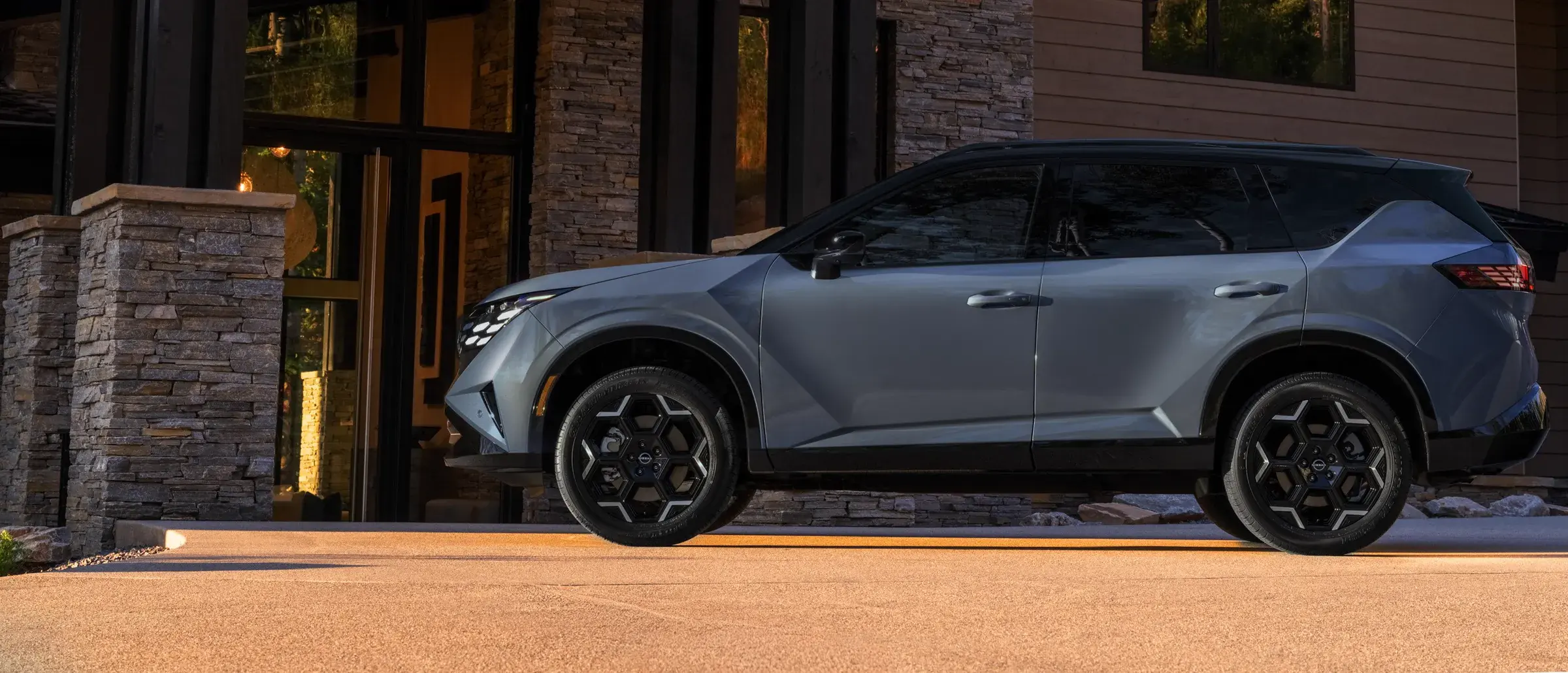 Nissan Rogue Hybrid vu de profil, stationné dans une entrée résidentielle contemporaine à la tombée du jour.