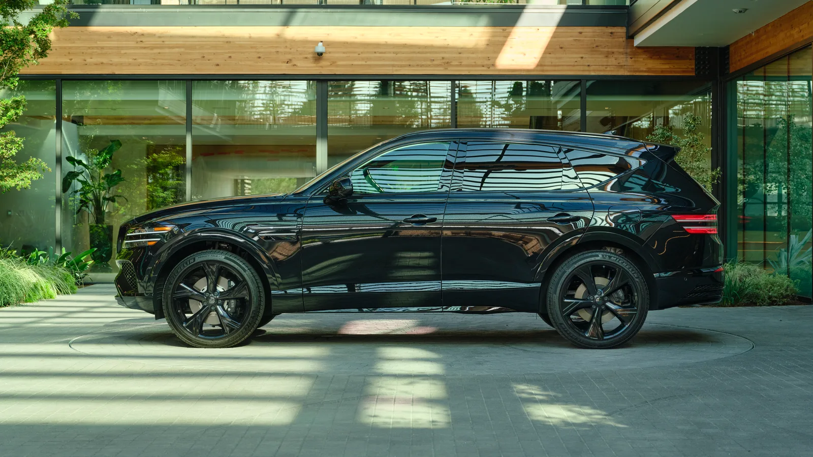 Genesis GV80 2027 noir vu de profil devant une façade vitrée, véhicule entier et roues visibles.