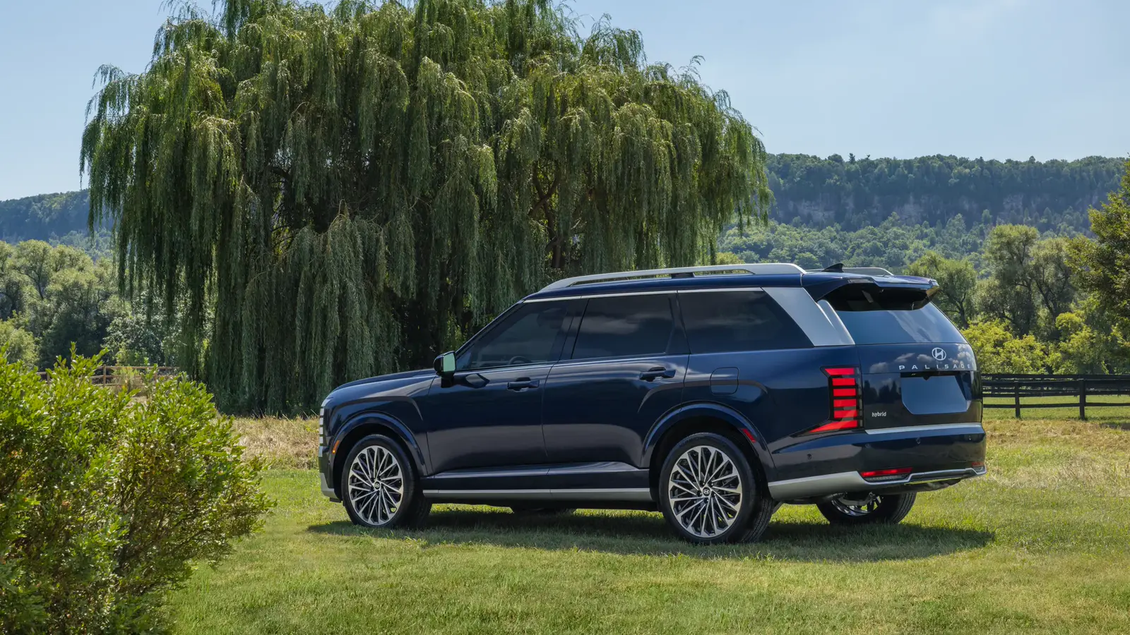 Hyundai Palisade 2026 bleu foncé entier vu de trois quarts arrière sur une pelouse, devant une clôture et des saules.