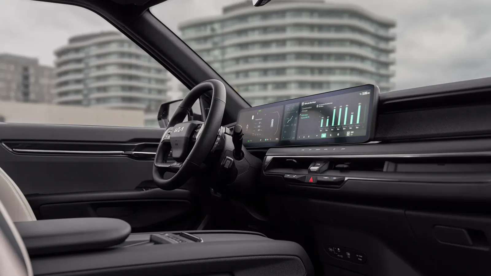 Poste de conduite d’une Kia EV9 2024, volant à logo Kia, écrans panoramiques et console centrale grise.